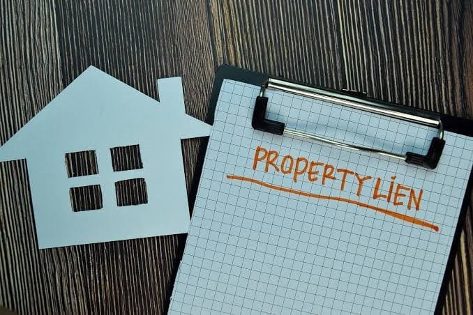 : Paper cutout of a house next to a clipboard with the words property lien written on it